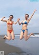 Two women in bikinis jumping in the air on the beach.