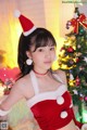 A woman in a santa outfit posing in front of a Christmas tree.