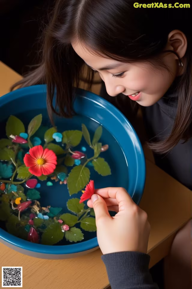 A young girl holding a red flower in a blue bowl.
