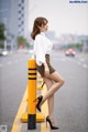 A woman leaning against a yellow pole on the side of the road.