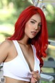 A woman with long red hair wearing a white bra top.