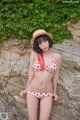 A woman in a bikini and straw hat posing on a rock.