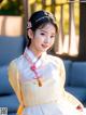 A woman wearing a yellow and white hanbok sitting on a couch.