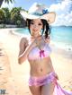 A woman in a bikini and hat on the beach.