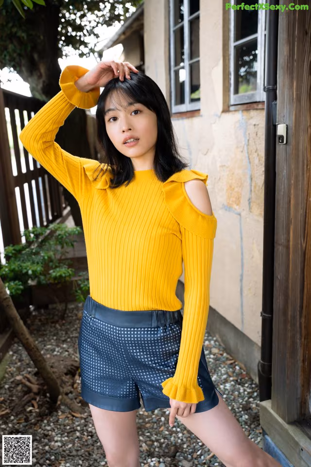 A woman wearing a yellow sweater and blue shorts.