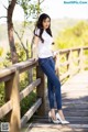A woman in a white shirt and blue jeans posing on a wooden bridge.