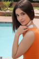 A woman in an orange bathing suit posing by a pool.