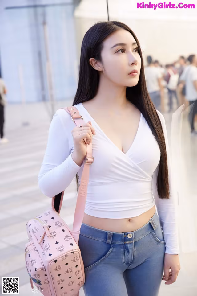 A woman in a white top and blue jeans holding a pink bag.