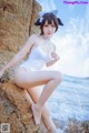 A woman in a white bathing suit sitting on a rock by the ocean.